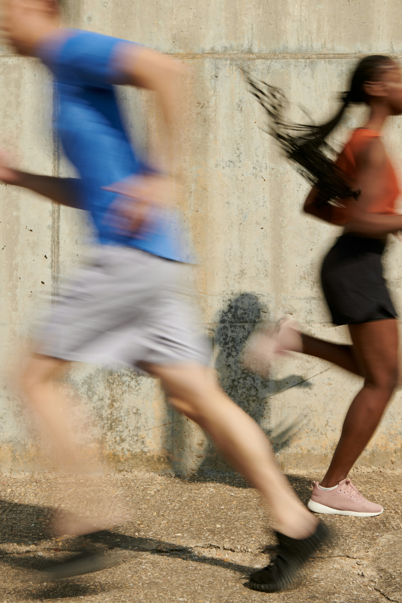 Two runners training outdoors against a concrete wall